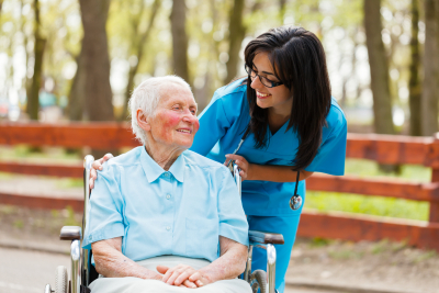 nurse and elderly lady in wheelchair chatting outdoors.